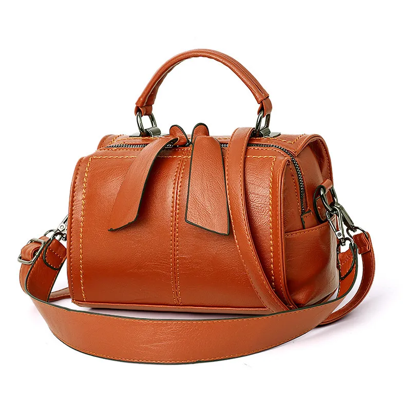 Cognac rounded handbag with a top handle, long strap and two dangling zipper pulls