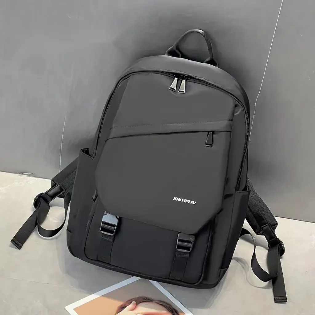 Dyed Black backpack, front view, showing the front flap, two buckle straps, and pockets