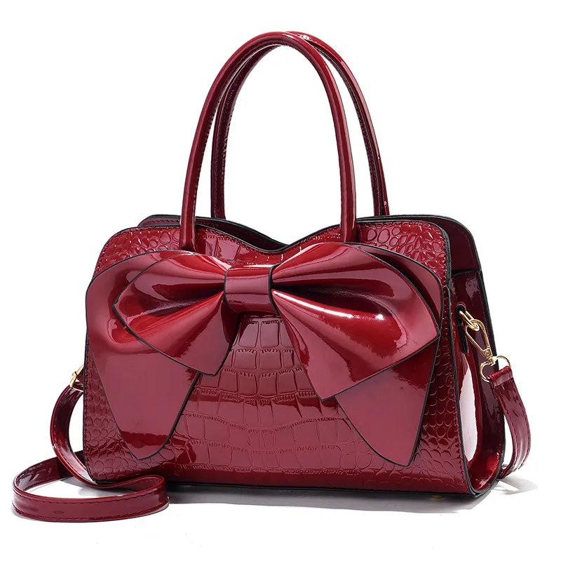 Wine croc-embossed handbag with a glossy front bow and long strap.